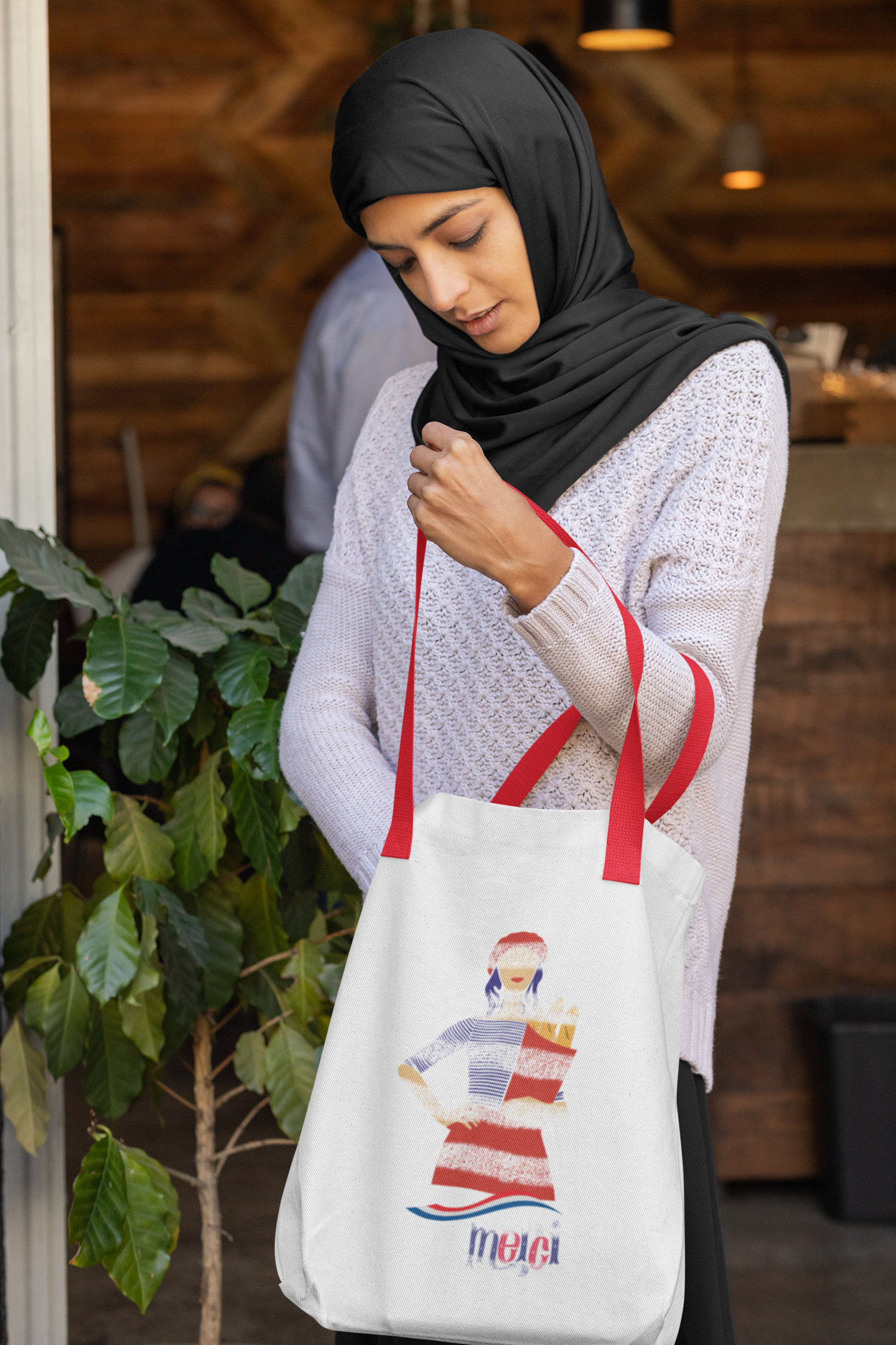 Woman holding a tote bag with a design and text, standing indoors.